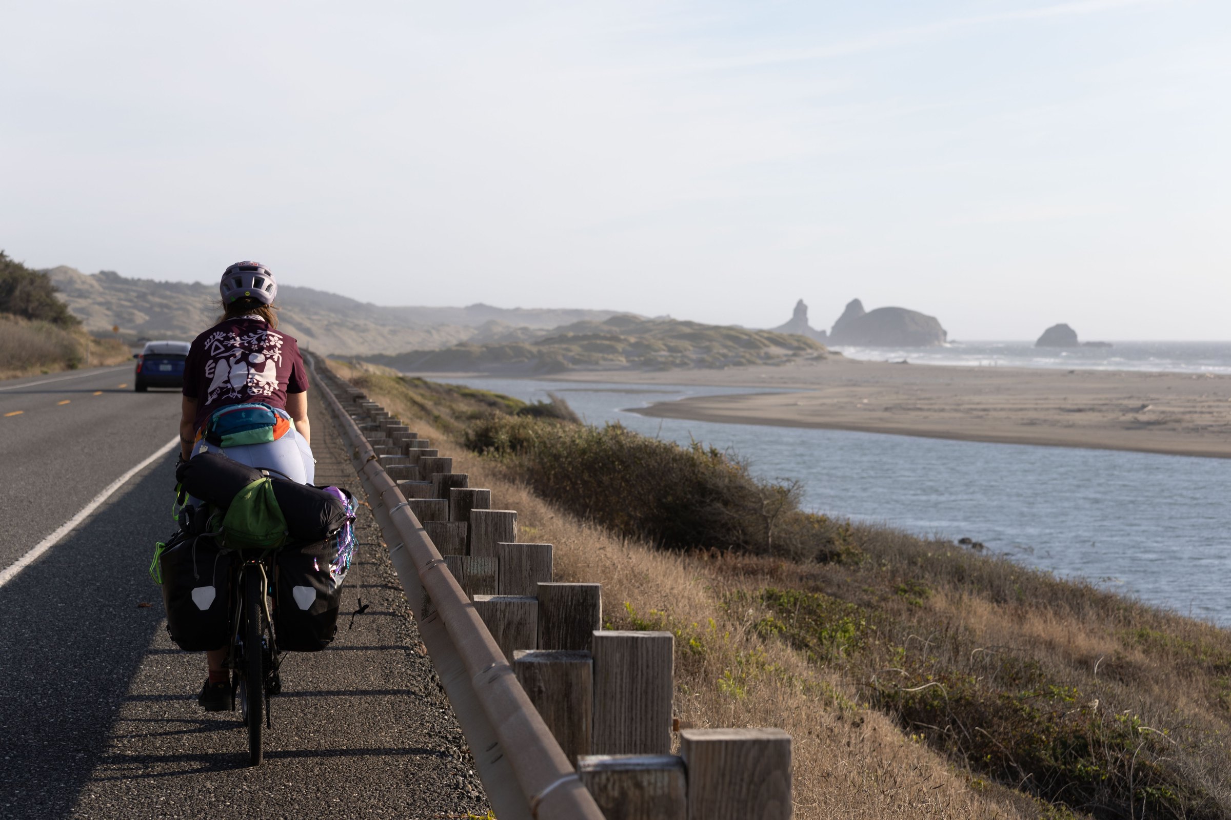 Bailey riding her touring bike beside the beach and sea stacks