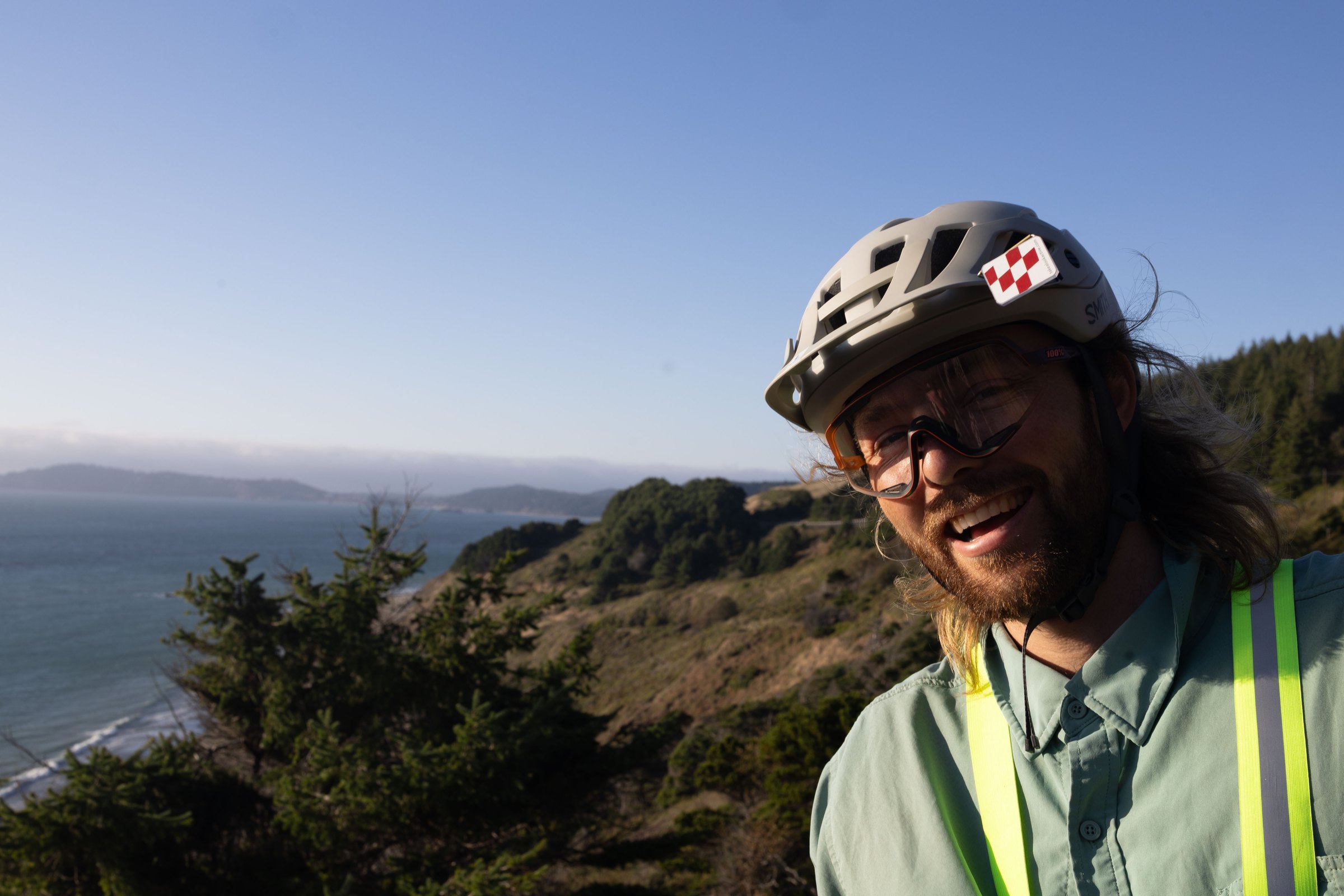 Keane smiling in his cycling helmet above the Pacific coast